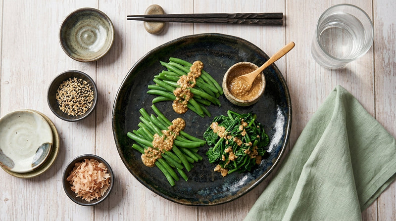 Haricots verts et épinards à la sauce sésame dans une assiette sombre, avec bonite séchée et graines de sésame